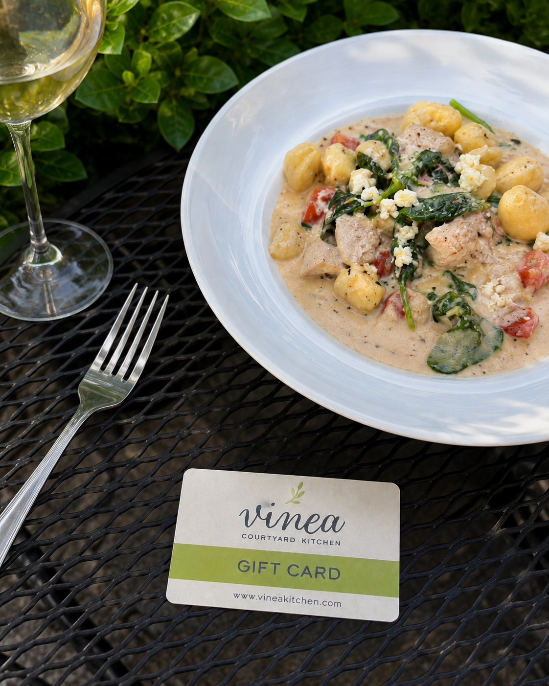 Vinea gift card beside gnocchi and wine in the courtyard